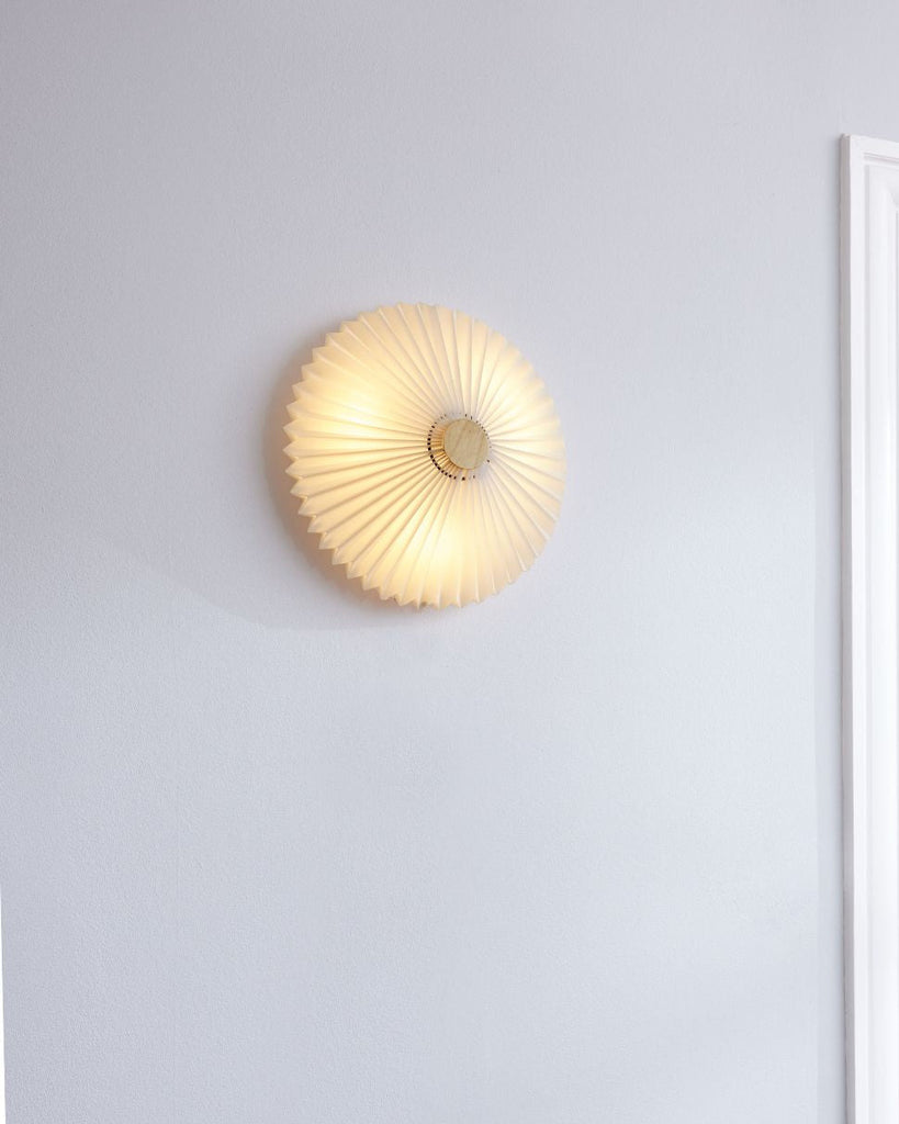 Round wall light fixture on a light gray wall with a mirror reflecting part of the room.